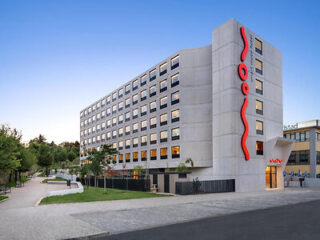 Modern hotel exterior with a distinctive red artwork on the facade, adjacent to a landscaped walkway.