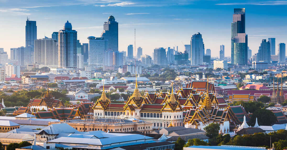 Panoramic view of Bangkok skyline at sunrise, highlighting the contrast between traditional Thai architecture of the Grand Palace and modern skyscrapers.