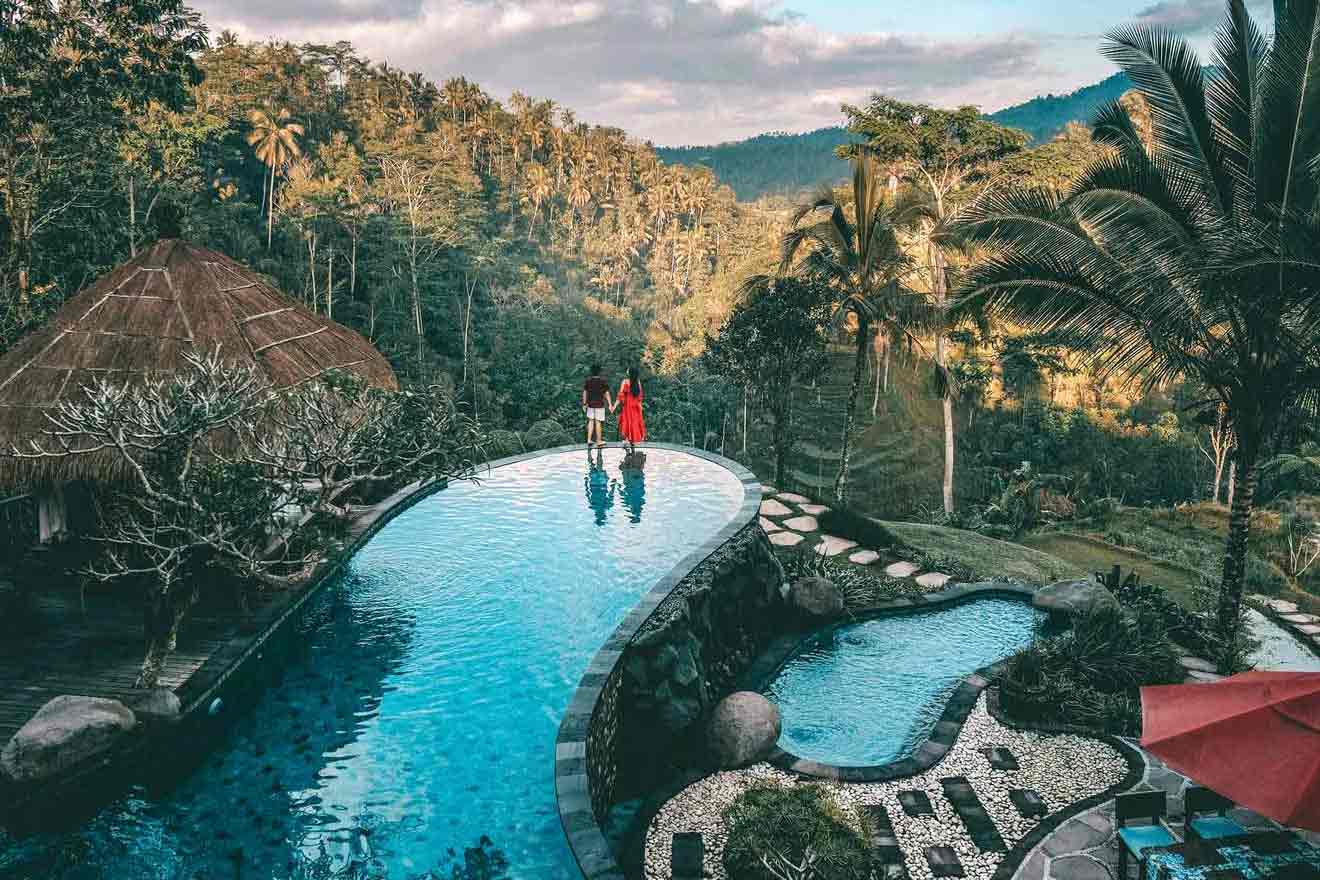 Two people standing on the edge of a pool in the jungle.