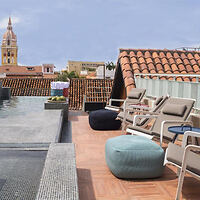 Rooftop terrace with a view of historic city architecture, featuring a pool, sun loungers, and shaded seating areas