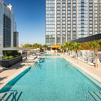 Hotel pool area with lounge chairs and a clear blue swimming pool flanked by a tall building