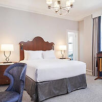 A classic and elegant room with a plush bed with a carved wooden headboard, luxurious bedding, flanked by sophisticated lamps