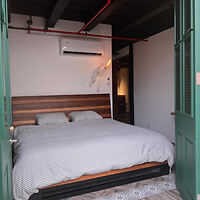 Minimalist bedroom with a rustic touch at Corcho Rooms, featuring a cozy double bed, wooden headboard, and modern air conditioning unit