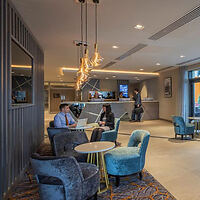 A modern hotel lounge area with guests, plush seating, and chic pendant lighting.