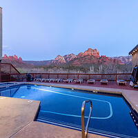 Outdoor swimming pool at twilight with Sedona's red rock formations in the background and multiple lounge chairs on the deck