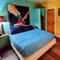 Bedroom with eclectic decor featuring a large mural over the bed, colorful bedding, and unique wall art