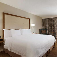 A clean, well-lit hotel room with a large bed with white linens, flanked by nightstands and a decorative headboard