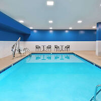 Indoor hotel pool with bright blue water, surrounded by blue and white walls and multiple chairs