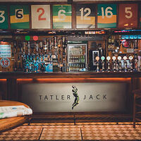 Quaint pub interior with a well-stocked bar under vintage scoreboards, named 'Tatler Jack'