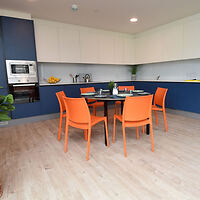 A contemporary kitchen dining area with bright orange chairs and a minimalist design.