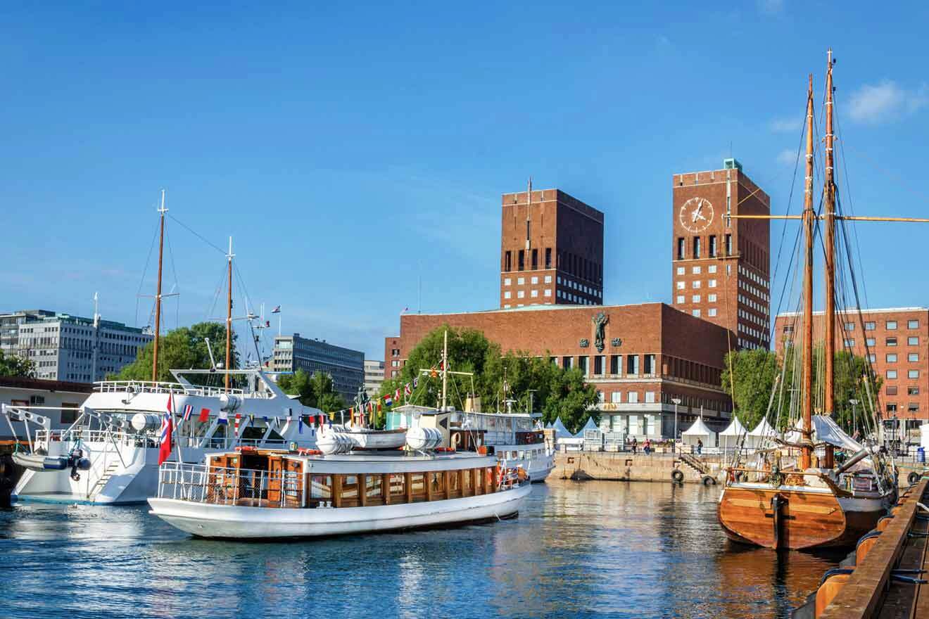 Oslo harbor view with a variety of boats docked near the iconic red brick City Hall building under a clear blue sky.