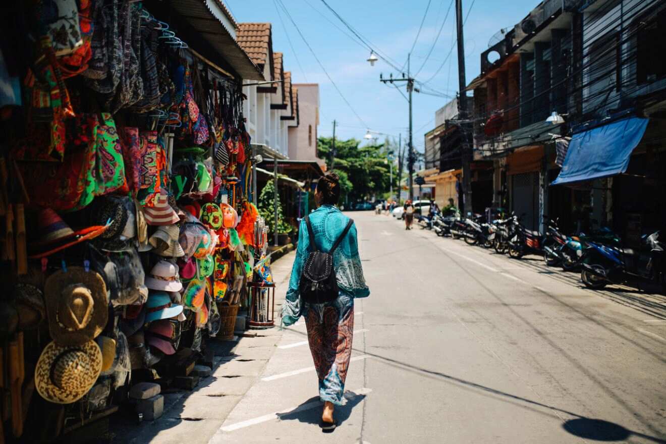 A colorful street market scene with in Thong Sala, Koh Phangan a variety of vibrant textiles and hats on display, and a person walking away in bright blue attire