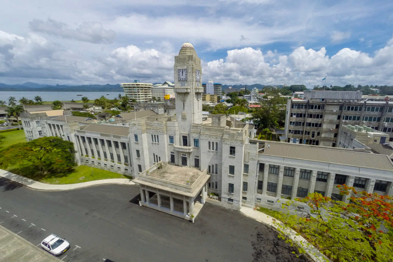 A historic, monumental building with classic architecture, seen from an aerial perspective, set against a backdrop of ocean and mountains in the distance