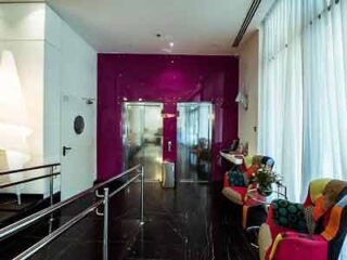 Hotel lobby with vibrant fuchsia walls, modern furniture with colorful upholstery, and sheer white curtains.