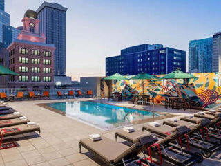 R ooftop pool area with colorful lounge chairs, umbrellas, and a vibrant mural on the backdrop of city buildings