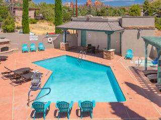 Hotel pool area with turquoise waters, patio chairs, and umbrellas with Sedona's red rocks visible in the distance