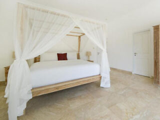 Minimalistic white bedroom with a large four-poster bed draped in sheer fabric, accented with a red cushion