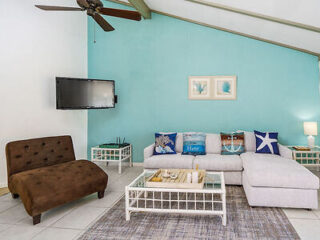 A welcoming living room with a large L-shaped sofa adorned with blue sea-themed cushions, a brown futon, and a flat-screen TV mounted on a light aqua wall