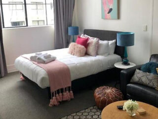 A stylish studio bedroom with a plush bed, pink and grey accents, and a chic sitting area