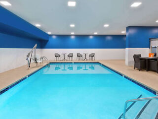 Spacious indoor swimming pool with clear blue water, surrounded by tables and chairs with a handicap-accessible pool lift