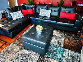 Chic downtown condo living area with black leather sofas adorned with blue and red cushions, a central black ottoman, and a textured multicolored rug