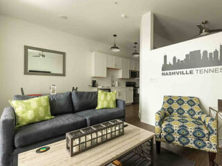 Cozy living area with a gray sofa, patterned armchair, and a white kitchen in the background, featuring a 'Nashville Tennessee' wall graphic