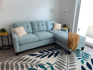 Modern cozy apartment living room featuring a light blue sofa with decorative pillows, a patterned area rug, and clean, simple decor