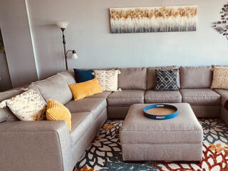 A comfortable living room in an oceanfront condo, featuring a large sectional sofa with decorative pillows, a patterned rug, and abstract wall art