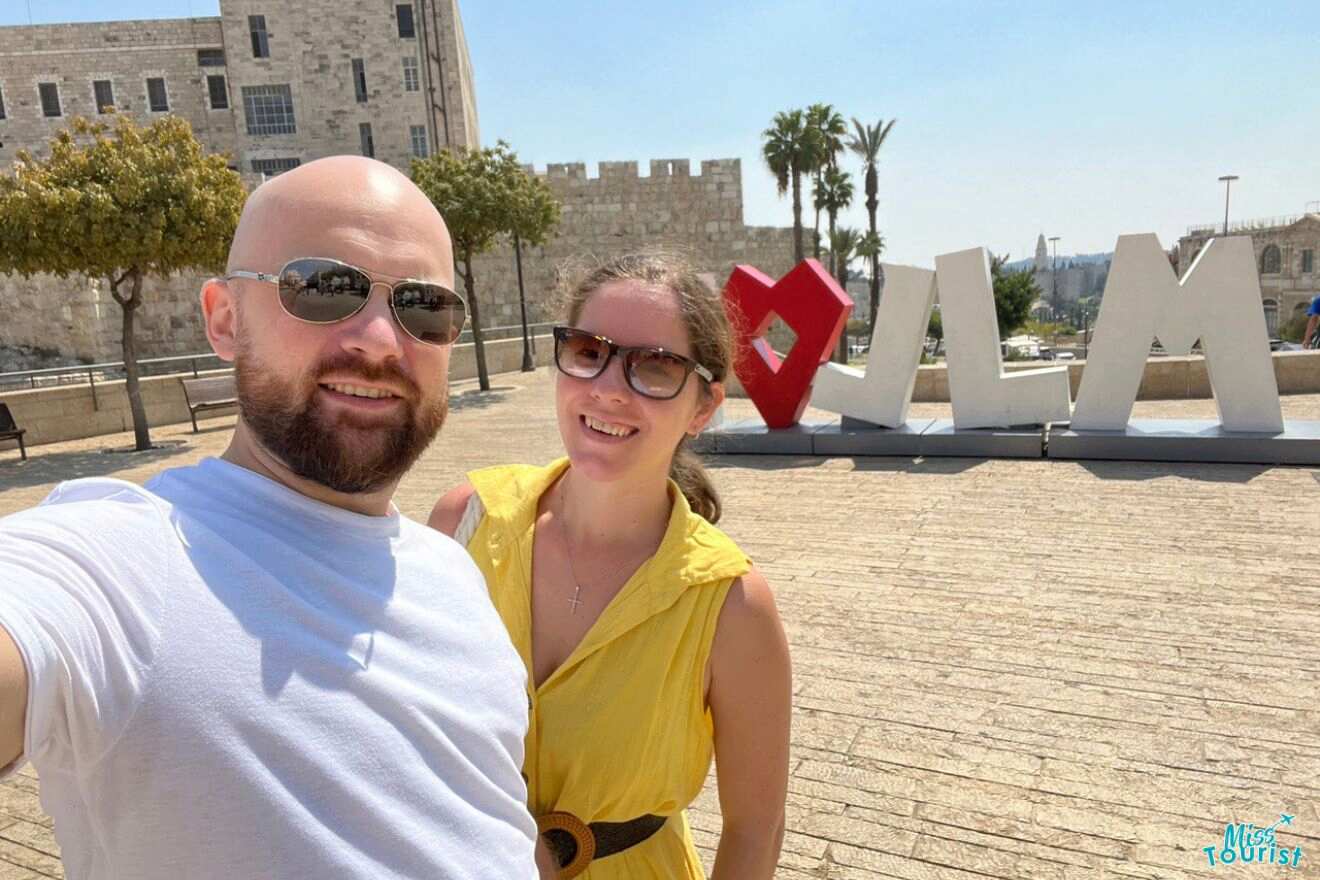 The writer of this post and her partner taking a selfie with a large 'I love JLM' sign in the background on a sunny day with historical buildings and palm trees.