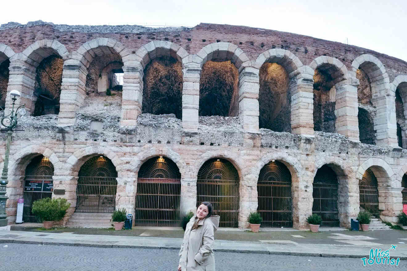 One of the MissTourist team members standing in front of the ancient Roman amphitheater in Verona, Italy, with visible arches and stone structures.