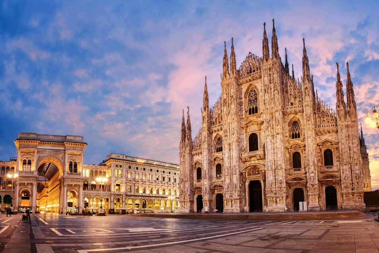 Twilight descends on Milan's Piazza del Duomo, casting a warm glow on the marble façade of the cathedral, with the grand arches of the Galleria Vittorio Emanuele II to the left, all under a soft pink and blue sky