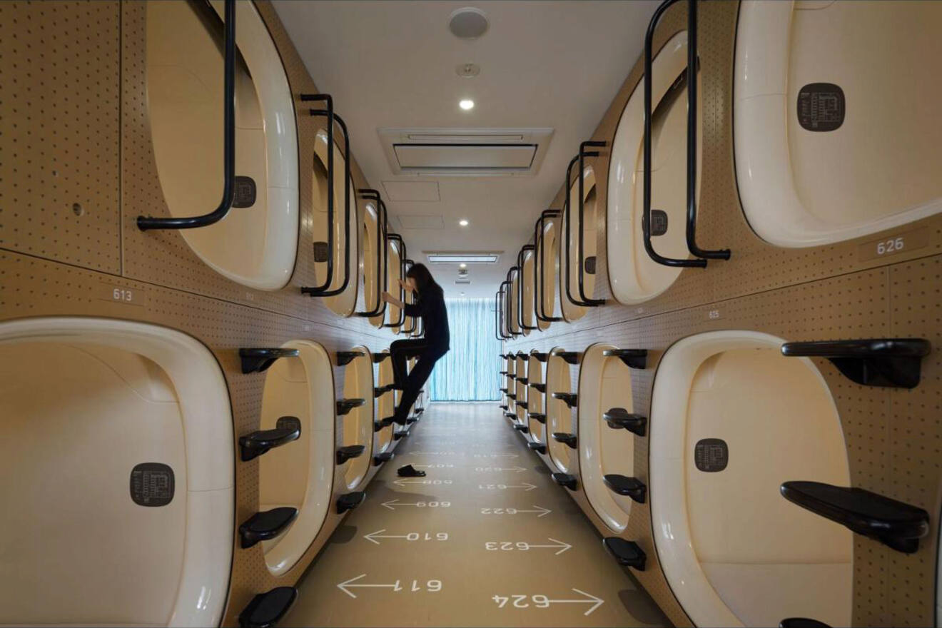 Interior of a modern capsule hotel in Tokyo with rows of sleeping pods and a person in the aisle