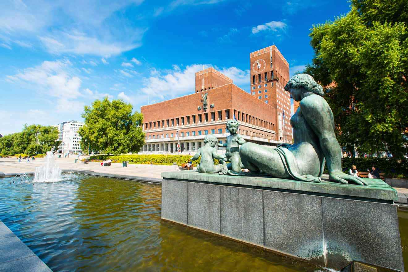 Oslo City Hall with historical statues in the foreground, blue skies and fountain, a symbol of the city's architectural heritage and civic pride.