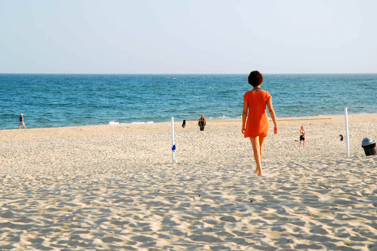 A woman in an orange dress walking towards the ocean on East Hampton Beach, depicting a relaxed beach experience in the Hamptons
