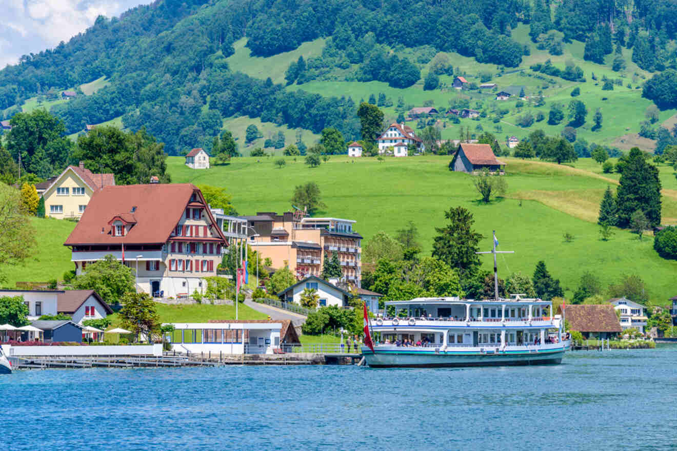 Scenic view of a steamboat cruising by Swiss lakeside houses with rolling green hills in the background, under a clear blue sky
