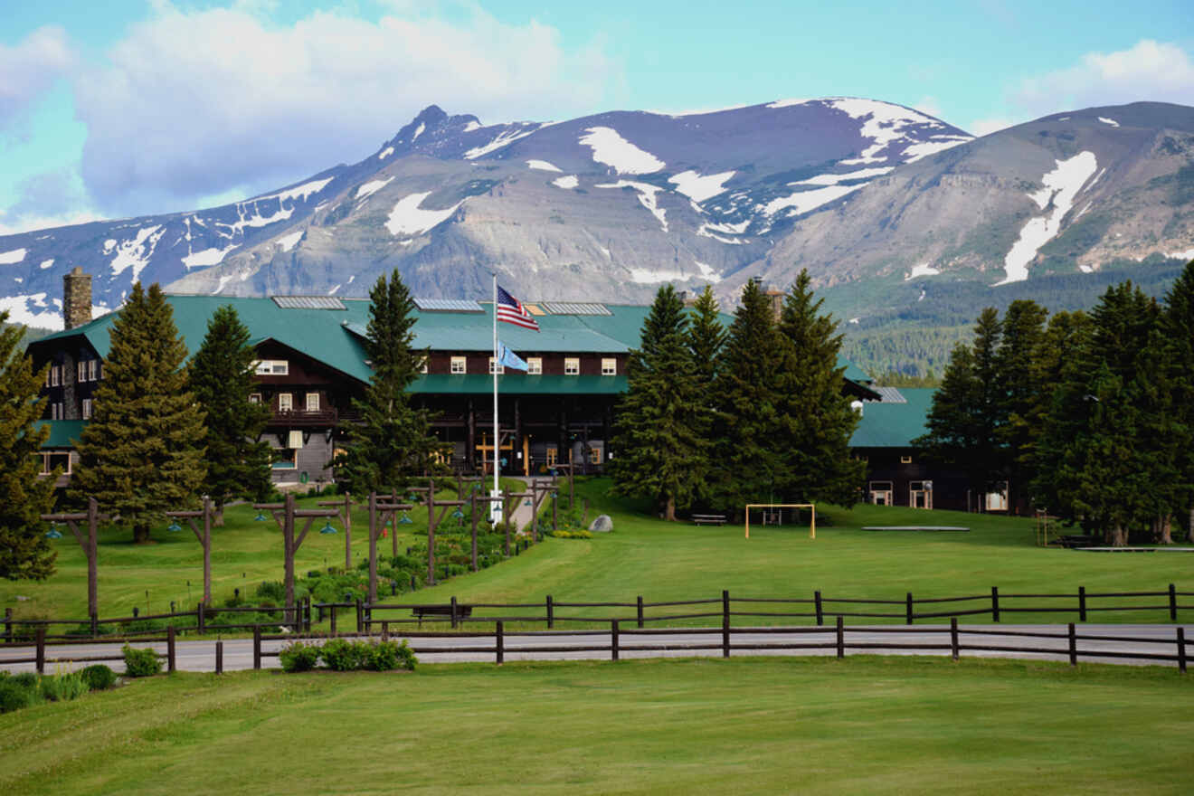Large rustic lodge with green roofs on a golf course, with towering mountains in the background and a partly cloudy sky
