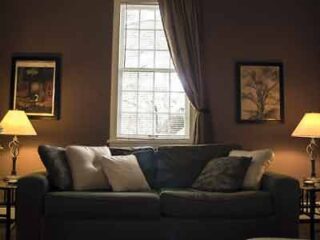 A dimly lit, cozy living room featuring a plush sofa, elegant table lamps, and framed artwork, offering a comfortable retreat.