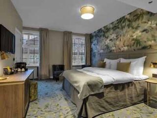 Hotel room with a green botanical wallpaper design, luxurious bedding, and classic furniture, providing a cozy and stylish atmosphere.