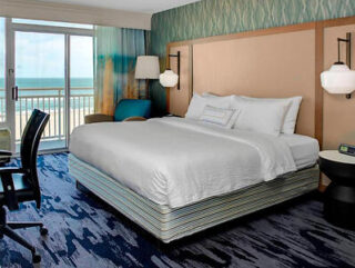 A serene hotel bedroom at the Fairfield Inn & Suites, with a plush king-size bed, balcony overlooking the ocean, and tasteful beach-themed decor.
