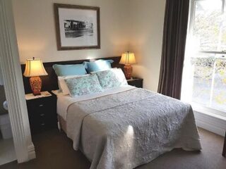 Comfortable guest room featuring a queen bed with teal and floral pillows, warm lighting from table lamps, and a view outside