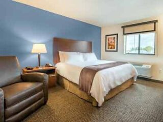 A hotel bedroom with a large bed, white linens, blue bed runner, and a comfortable armchair, offering a welcoming atmosphere for guests.