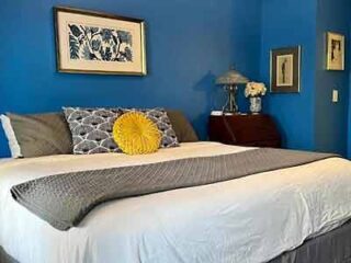 A bedroom with a deep blue accent wall, grey tufted headboard, and decorative framed art, creating a tranquil sleeping space.