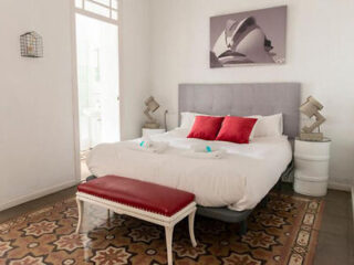 Comfortable bedroom with a plush bed, red accents, and traditional Spanish floor tiles