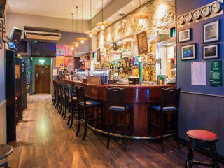 A traditional bar interior with a wooden counter, stools, and a variety of framed pictures and mirrors on the wall