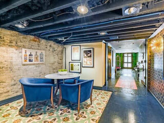 Chic hallway with exposed brick walls, blue velvet chairs, and eclectic floor tiles, leading to a bright entryway