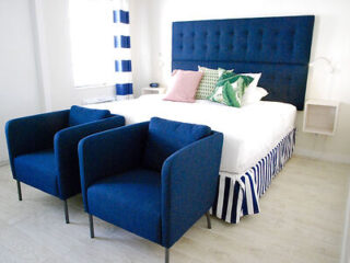 Bright and airy bedroom with a deep blue upholstered headboard, matching armchairs, and striped bed linen