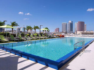 Outdoor hotel pool with clear blue water, green lounge chairs, and a view of the Tampa skyline