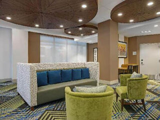 Modern hotel lobby with patterned blue carpet, lime green armchairs, and decorative overhead lighting