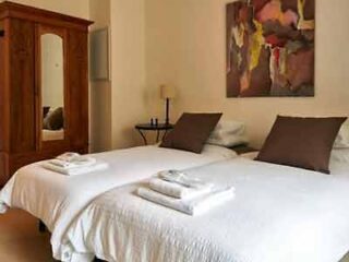 Cozy hotel room with two single beds dressed in white linen, a wooden wardrobe, and a large abstract painting on the wall.