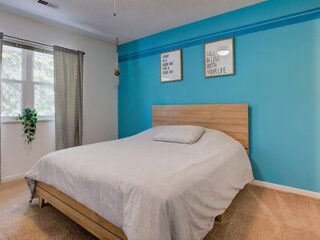 Bright bedroom with a queen-sized bed, light hardwood floors, and a blue accent wall with decorative quotes